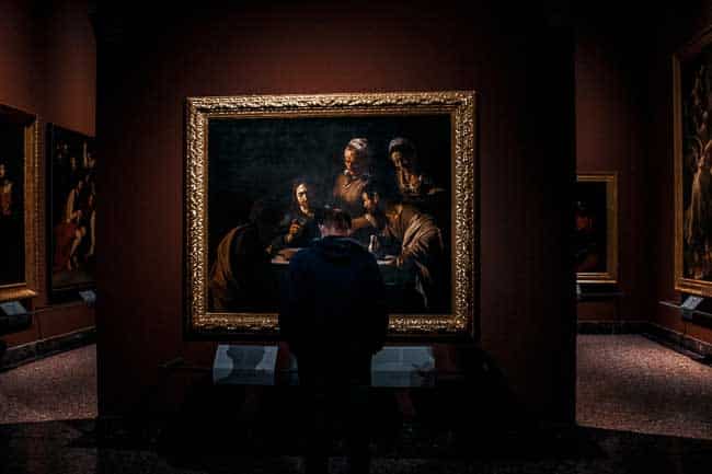 A man wearing a mask stands in front of and contemplates the Milan version of Caravaggio’s The Last Supper painting in the Brera Gallery in Milan