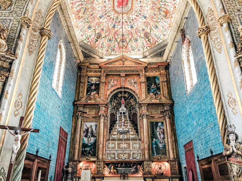 The altar of a chepel with bright blue tiled walls and a tiled ceiling with intricate patterns at Saint Michaels Chapel in Coimbra University
