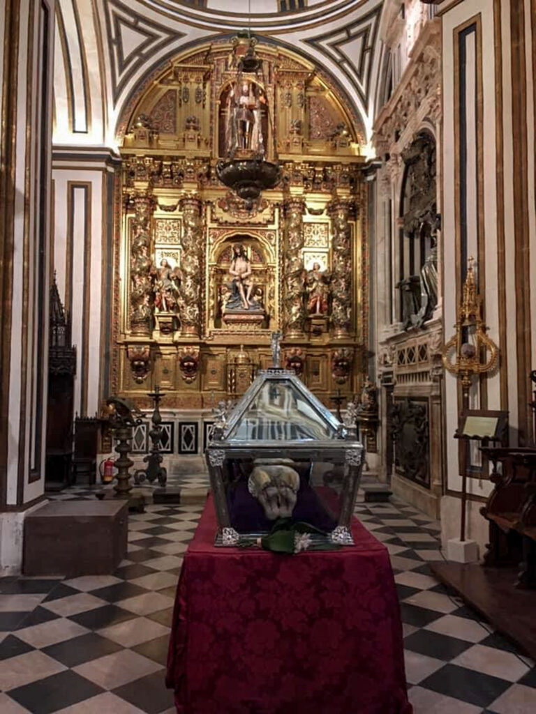 The Interior of the Burgos Cathedral with intricate gold details on a huge altar with a checkered patterned floor.