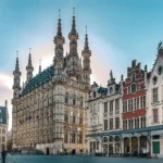 A view of the main square in Leuven, Belgium with the spires almost like mosque minarets of the City Hall Stadhuis and some of the restaurants against a blue sky in Leuven, Belgium