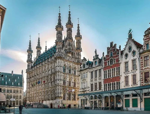 A view of the main square in Leuven, Belgium with the spires almost like mosque minarets of the City Hall Stadhuis and some of the restaurants against a blue sky in Leuven, Belgium
