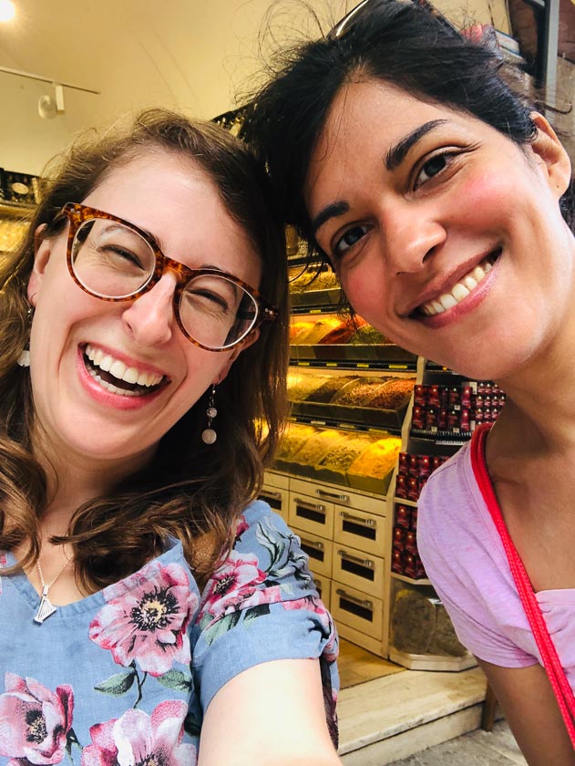 Two young women are smiling and putting their heads together for a selfie in Istanbul. One wears a flower top, the other pink.
