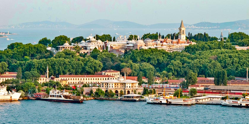 Aerial view of Topkapi Palace surrounded by lush greenery, with boats docked along the waterfront in Istanbul.