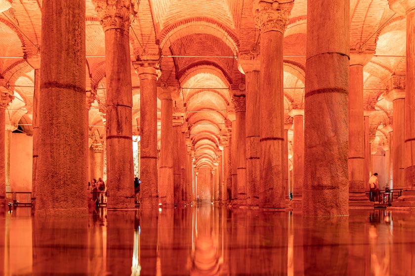 Interior view of the Basilica Cistern in Istanbul, featuring rows of illuminated columns reflected in the shallow water.