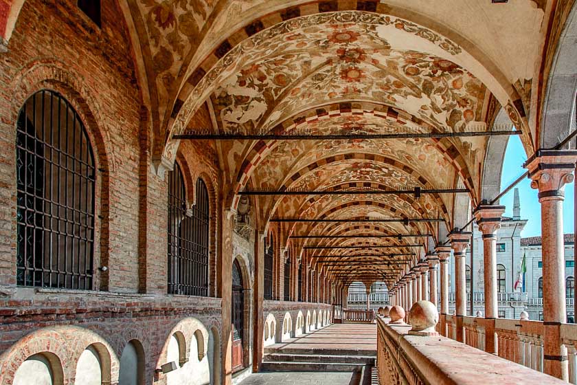 Part of the upper gallery of the Palazzo della Ragione in Padua Italy with lots of thin columns to the right and beautiful medeival florals adorning the upper arches.