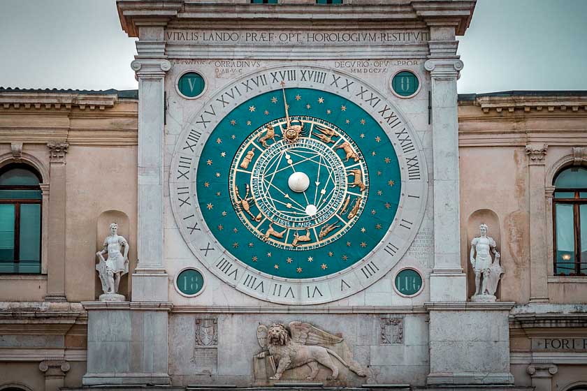 The clock tower in the Piazza del Signori where you can have dinner in Padua. A round blue clock in a square marble facade. 