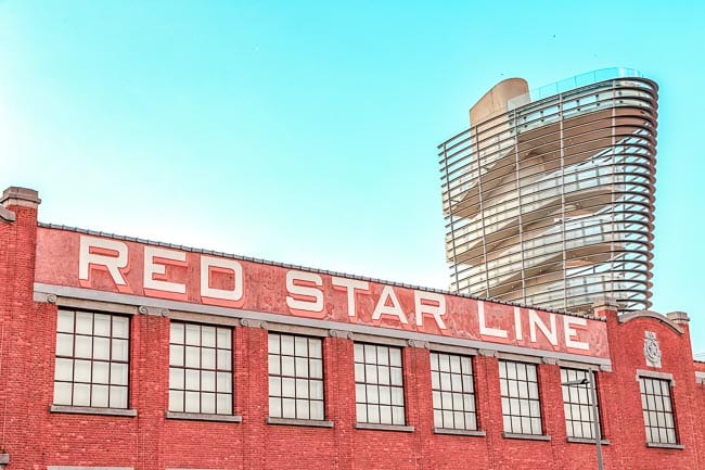 The exterior of the Red Star Line museum in Antwerp - a red brick buildling with the words “Red Star Line” in old fashioned lettering on top, all against a blue sky. Antwerp has amazing museums that should be visited on your one day in Antwerp.
