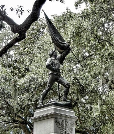 A statue in Oglethorpe Square in Savannah, GA with live oak trees surrounding it with moss. The statue is holding and waving a flag. Seeing the historic squares of Savannah is one of the best things to do in Savannah in one day!