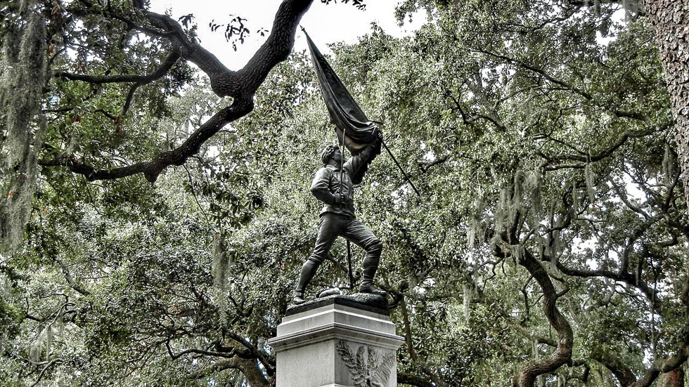 A statue in Oglethorpe Square in Savannah, GA with live oak trees surrounding it with moss. The statue is holding and waving a flag. Seeing the historic squares of Savannah is one of the best things to do in Savannah in one day!